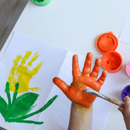 Child painting a hand with orange paint to make a colorful flower handprint craft — fun and easy printable handprint art project from Mr. Mintz for preschoolers, toddlers, and kindergarten classrooms